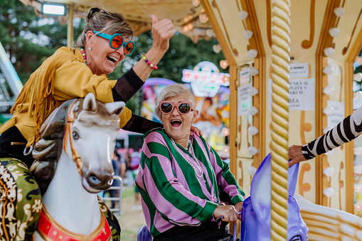 Happy senior friends enjoying county fair at carousel.